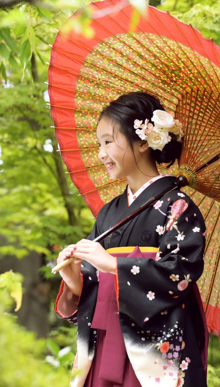 新緑の屋外ロケーションで和傘を差して、笑顔の女の子。